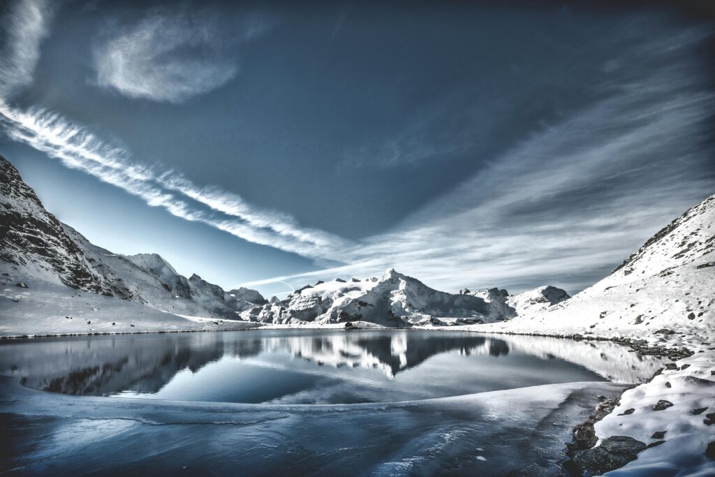 A breathtaking view of a snowy mountain lake reflecting the sky, with serene winter scenery.